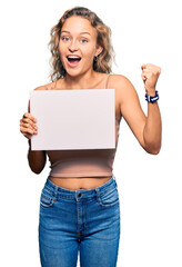 Naklejka premium Beautiful caucasian woman holding blank empty banner screaming proud, celebrating victory and success very excited with raised arms