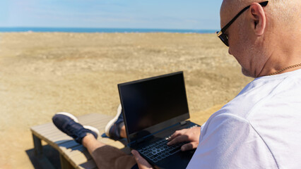 on a sunny day, a man works on his laptop on a beach by the sea