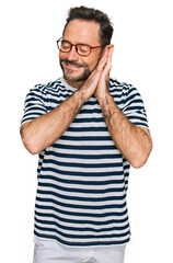 Middle age man wearing casual clothes and glasses sleeping tired dreaming and posing with hands together while smiling with closed eyes.