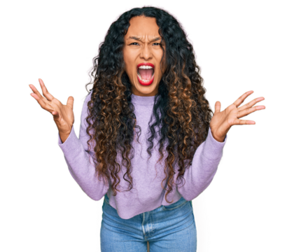 Young hispanic woman with curly hair wearing casual winter sweater crazy and mad shouting and yelling with aggressive expression and arms raised. frustration concept.