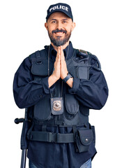 Young handsome man wearing police uniform praying with hands together asking for forgiveness smiling confident.