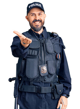 Young handsome man wearing police uniform smiling cheerful offering palm hand giving assistance and acceptance.