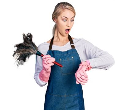 Beautiful young blonde woman wearing apron holding cleaning duster looking at the watch time worried, afraid of getting late