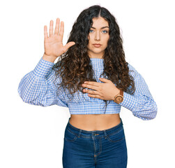 Young hispanic girl wearing casual clothes swearing with hand on chest and open palm, making a...