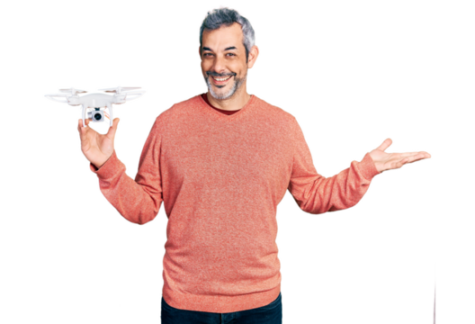 Middle age hispanic man with grey hair holding drone celebrating achievement with happy smile and winner expression with raised hand