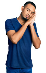 Fototapeta premium Young african american man wearing casual t shirt sleeping tired dreaming and posing with hands together while smiling with closed eyes.