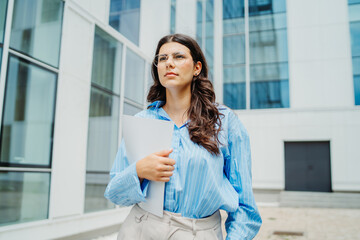 One beautiful young successful business woman going to work at business office modern building while holding papers and wearing glasses	