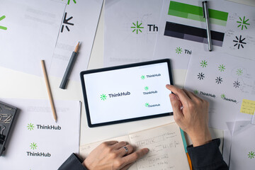 tabletop view of a logo design process, featuring sketches, color swatches, and digital drafts on a tablet. various design tools and materials, including pencils and markers.	