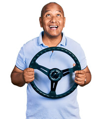 Hispanic middle age man holding steering wheel angry and mad screaming frustrated and furious,...