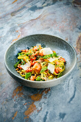 Traditionelle italienische Pasta mit grünem Spargel, Garnelen und geräucherten Lachsstreifen serviert mit Pinienkernen und Parmesan Scheiben als Nahaufnahme in einer Nordic Design Schale