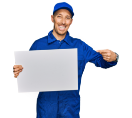 Bald man with beard wearing builder jumpsuit uniform holding empty banner smiling happy pointing with hand and finger