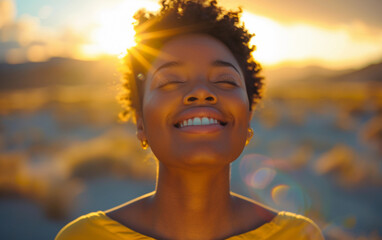 An African woman with short curly hair is smiling and looking upwards toward the setting sun