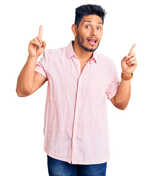 Handsome latin american young man wearing casual summer shirt smiling amazed and surprised and pointing up with fingers and raised arms.
