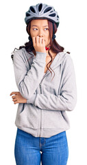 Young beautiful chinese girl wearing bike helmet looking stressed and nervous with hands on mouth biting nails. anxiety problem.