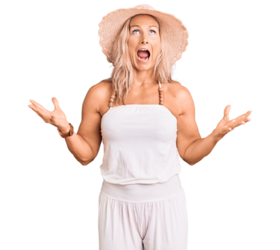 Middle age fit blonde woman wearing summer hat crazy and mad shouting and yelling with aggressive expression and arms raised. frustration concept.