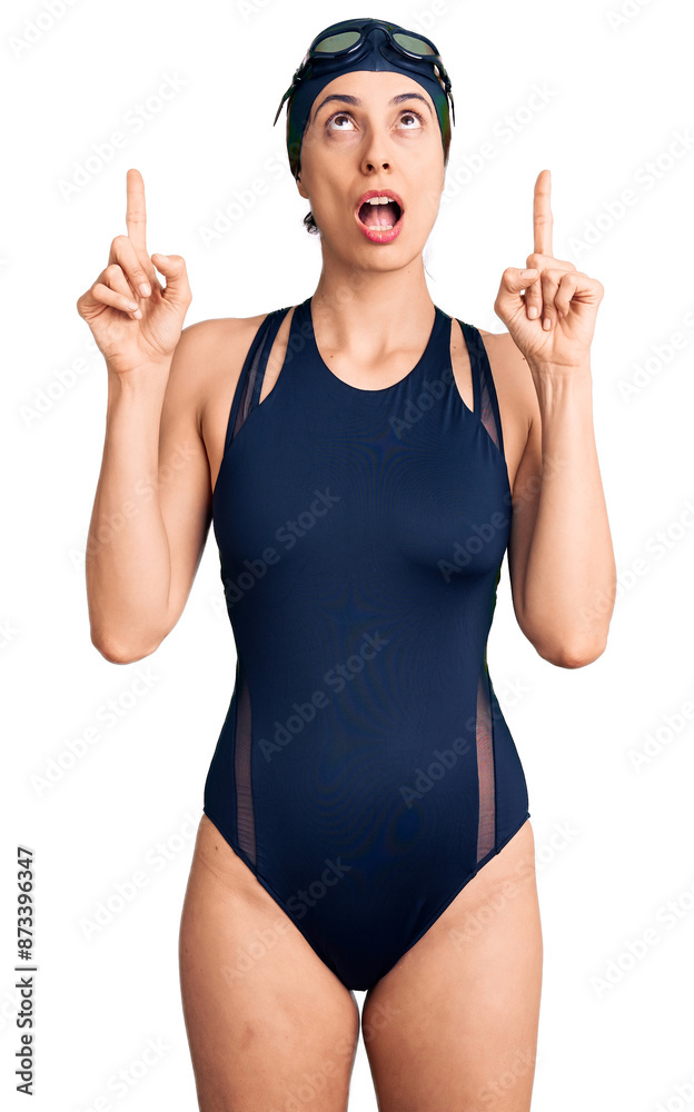 Wall mural young beautiful hispanic woman wearing swimwear and swimmer glasses amazed and surprised looking up 