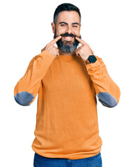 Hispanic man with beard wearing casual winter sweater smiling with open mouth, fingers pointing and forcing cheerful smile