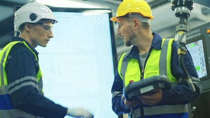 One techinican worker hold controller and also discuss with engineer for maintenance and control quality of work of robotic arm machine in factory.