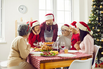 Happy big family with kids and grandparents in Santa Claus hat sitting at Christmas table holding festive cake celebrating new year or thanksgiving day at home. Holidays and celebration concept.