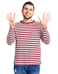 Young handsome man wearing striped sweater showing and pointing up with fingers number nine while...