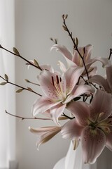 A bouquet of light pink lilies in a white vase, with some brown branches with green buds.

