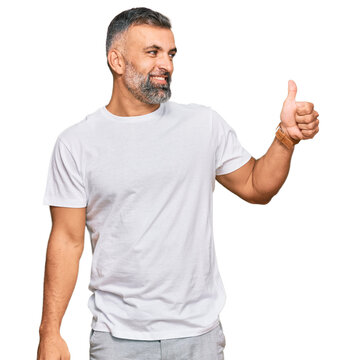 Middle age handsome man wearing casual white tshirt looking proud, smiling doing thumbs up gesture to the side