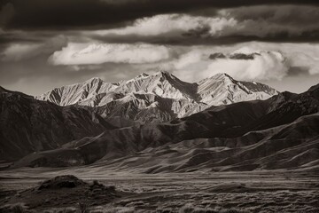 A black and white photo of a mountain range with a large cloud over the top.

