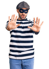 Young handsome man wearing burglar mask doing stop gesture with hands palms, angry and frustration expression