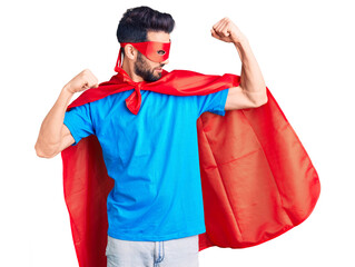 Young handsome man with beard wearing super hero costume showing arms muscles smiling proud....