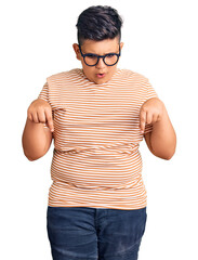 Fototapeta premium Little boy kid wearing casual clothes and glasses pointing down with fingers showing advertisement, surprised face and open mouth