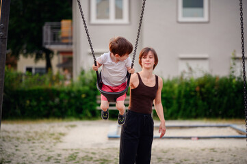 A mother pushing her young son on a swing at the playground, enjoying a fun and playful moment together outdoors.