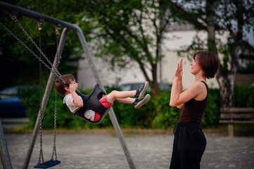 Obraz premium A mother pushing her laughing young son on a swing at the playground, capturing a moment of pure joy and playful bonding together outdoors.
