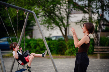 Obraz premium A mother pushing her laughing young son on a swing at the playground, capturing a moment of pure joy and playful bonding together outdoors.