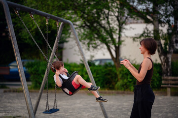 Obraz premium A mother pushing her laughing young son on a swing at the playground, capturing a moment of pure joy and playful bonding together outdoors.