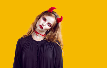 Portrait of creepy woman looking at you with creepy look on Halloween on orange background. Girl in black dress, red horns and imitation of cut throat looks at camera without smile. Halloween concept.