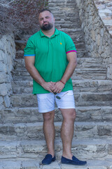 Relaxed Vacation Portrait of a Bearded Man in His 30s, Dressed in a Green T-Shirt and Light Shorts, Standing on Stone Steps