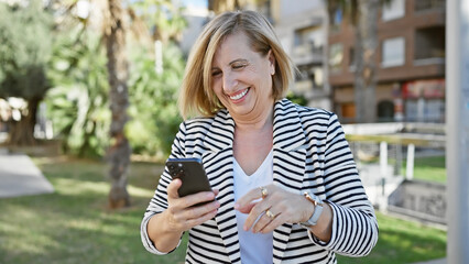 A smiling mature woman using a smartphone in a sunny park with palm trees