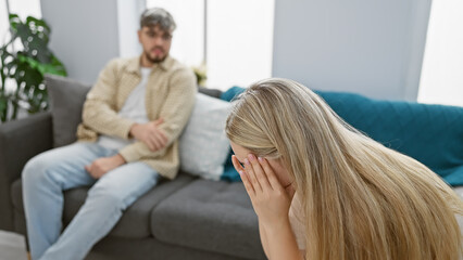Obraz premium A distressed woman crying in the foreground with a concerned man sitting on a couch in a modern living room.