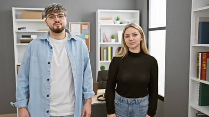 A man and woman stand confidently in a modern office, signifying a professional team.