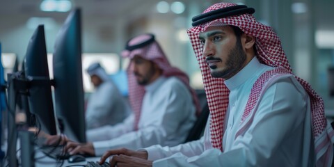 Focused Saudi Arabian men working on computers in an office environment wearing traditional attire