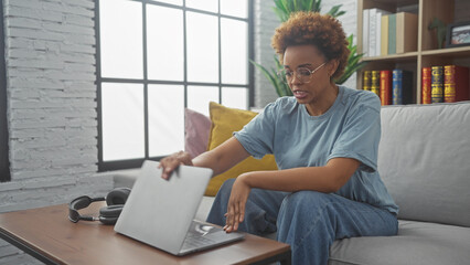 African american woman using laptop in a modern living room setup, depicting a casual work-from-home environment.