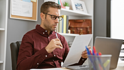 Hispanic man reading a document intently in a modern office setting, portraying professionalism and...