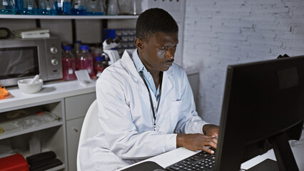 An african american man in a lab coat, focused while working at a computer in a laboratory setting.