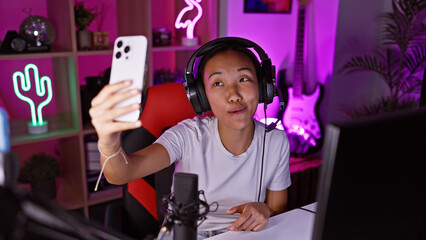 A young asian woman takes a selfie in a vibrant gaming room with neon lights and a microphone setup at night.