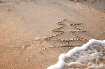 A New Year tree is drawn on the sea sand. Summer sea background