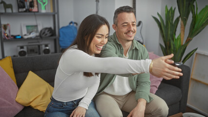 Obraz premium Cheerful couple taking a selfie in a cozy living room, depicting love and family life in a modern home setting.