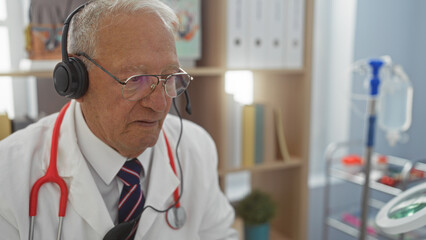 An elderly caucasian man with grey hair, wearing a headset and a stethoscope, works in a hospital...