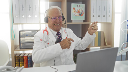 Elderly, caucasian, man, in, a, clinic, workplace, with, grey, hair, using, a, laptop, and, wearing, headphones, while, smiling.