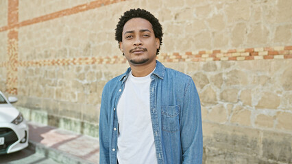 Obraz premium Handsome young adult man with curly hair wearing a denim jacket stands confidently on a city street.