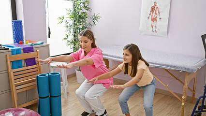 A pediatrician guides a young girl through exercises in a well-equipped physical therapy room.